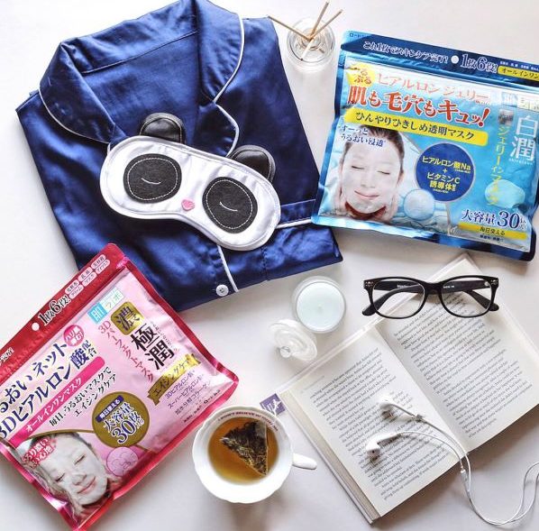 flatlay of hada labo products on a bedsheet with books, spectacles, cofee