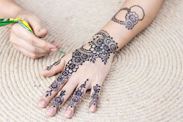 person drawing henna art on back of palm