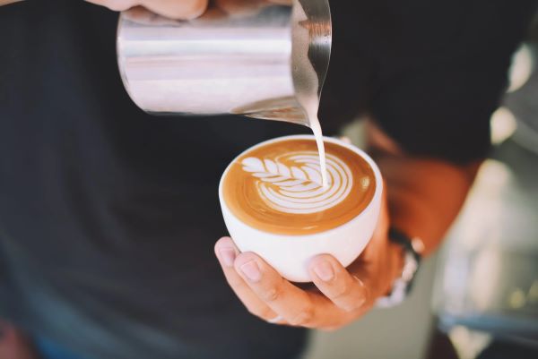 man holding a cup of coffee and making latte art