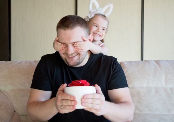 daughter covering father's eyes while surprising him with cake 