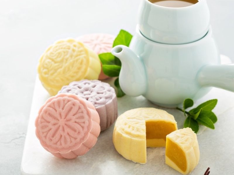 assorted snowskin mooncakes in purple, pink, and yellow on a plate with a pot of tea best snowskin mooncakes singapore
