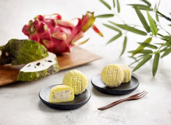 soursop snowskin mooncakes with yellow skin on black plates with fresh soursop and dragonfruit