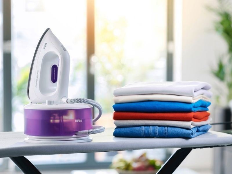 Braun lavendar Carestyle steam generator iron on an iron board next to pile of folded clothes