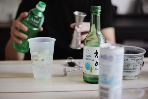 person holding a bottle at a table with soju on top 