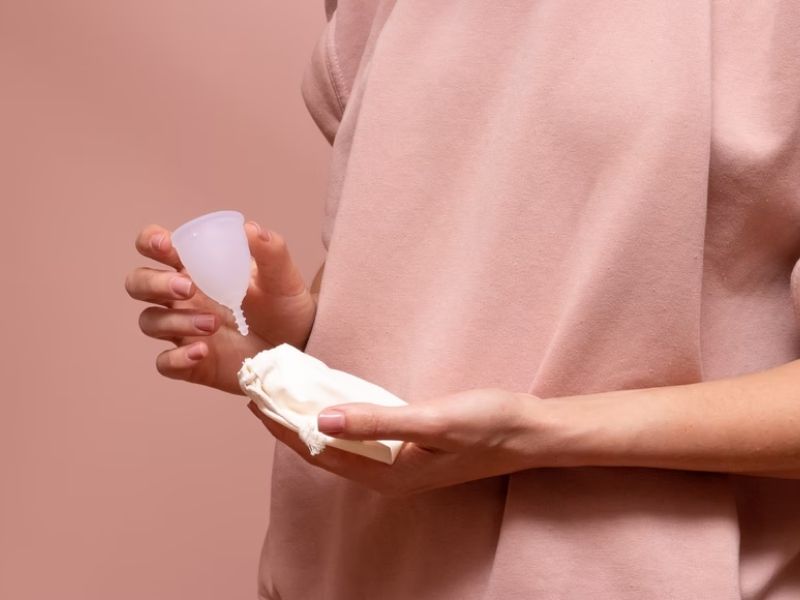 woman in pink shirt holding clear menstrual cup and pouch
