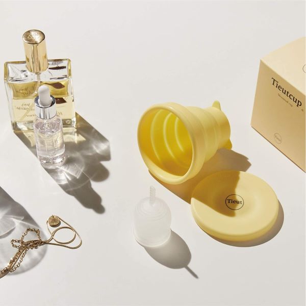 clear menstrual cup, yellow collapsible storage cup and perfume bottles on white background best menstrual cups singapore