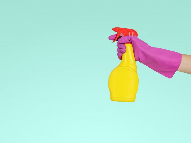 person holding yellow spray with pink gloves on blue background