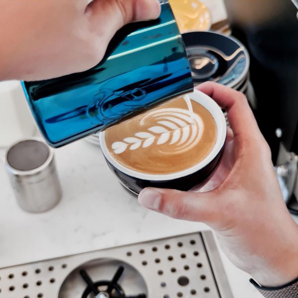 person making rosetta latte art with a blue frothing jug 