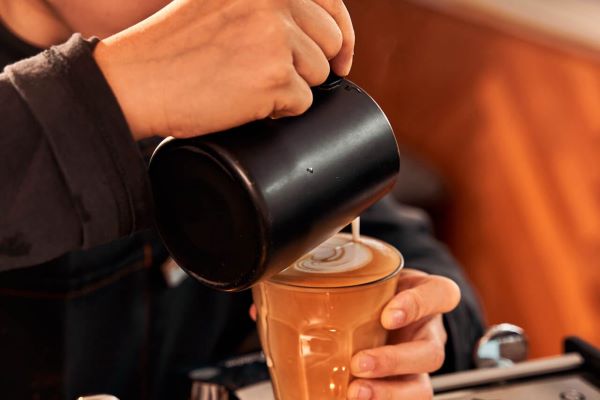 person pouring latte art with black frothing jug