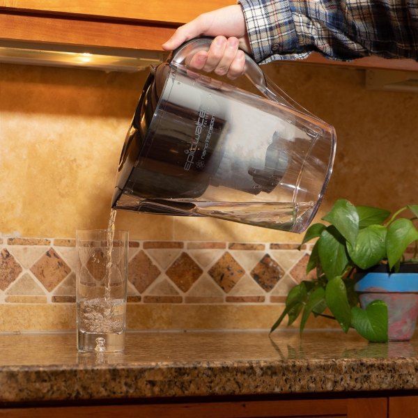 man pouring water through water filter jug pitcher into glass