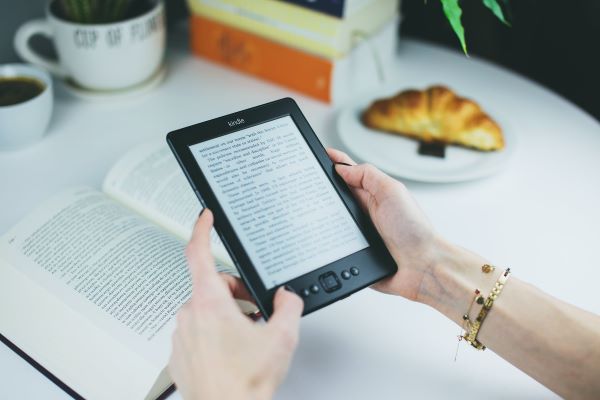 person holding a black kindle with page turn buttons 