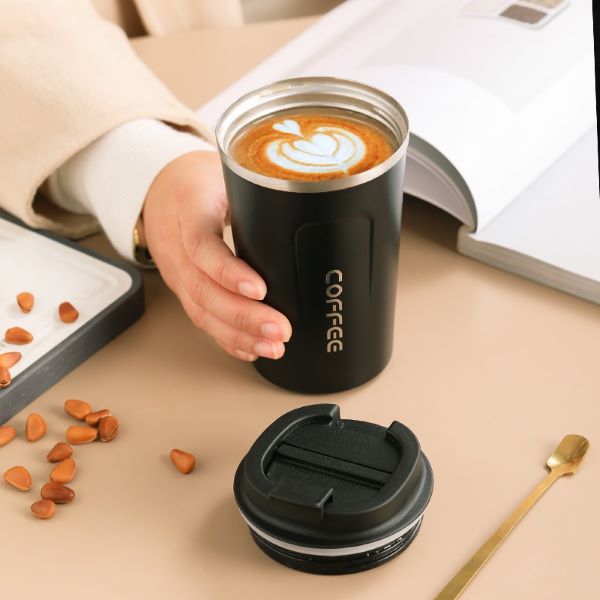 person holding a black tumbler with coffee inside