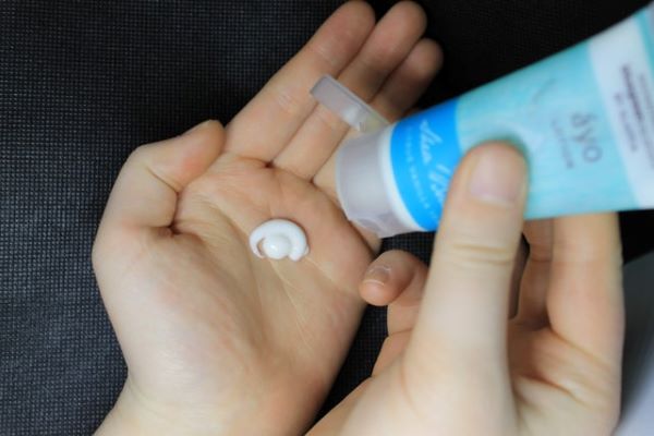 person squeezing a tube of moisturiser on palms
