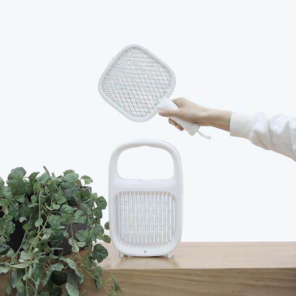 person holding a white mosquito electric swatter over a white lamp on a wooden table best mosquito killer singapore