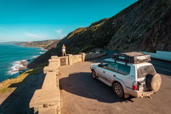 woman standing in front of car looking at views at great ocean road itinerary