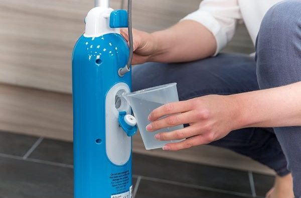 person pouring water into water tank of a steam mop