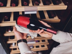 person holding a bottle of wine taken out from a wine chiller with wooden racks