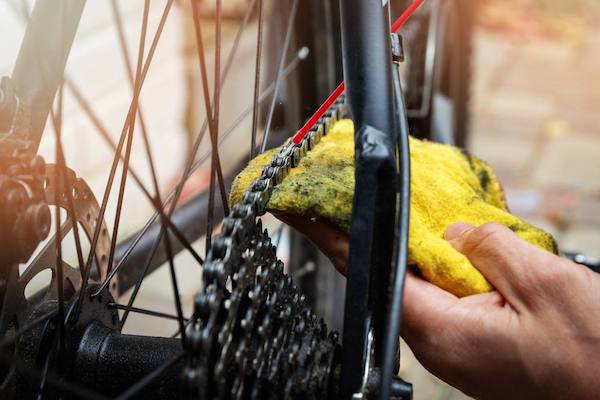person wiping bicycle chain clean with yellow rag