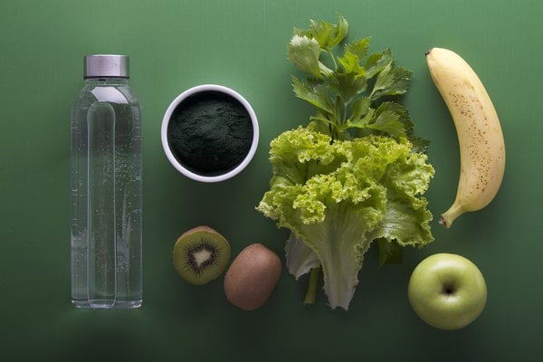 flat lay of water bottle, kiwi, and green vegetables