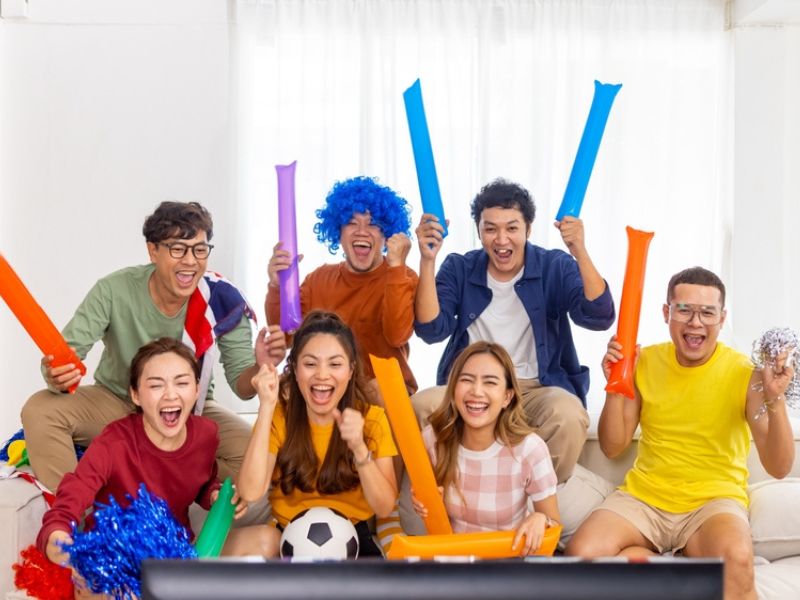 Group of Asian man and woman friends watching soccer games world cup competition on television with eating snack together at home.