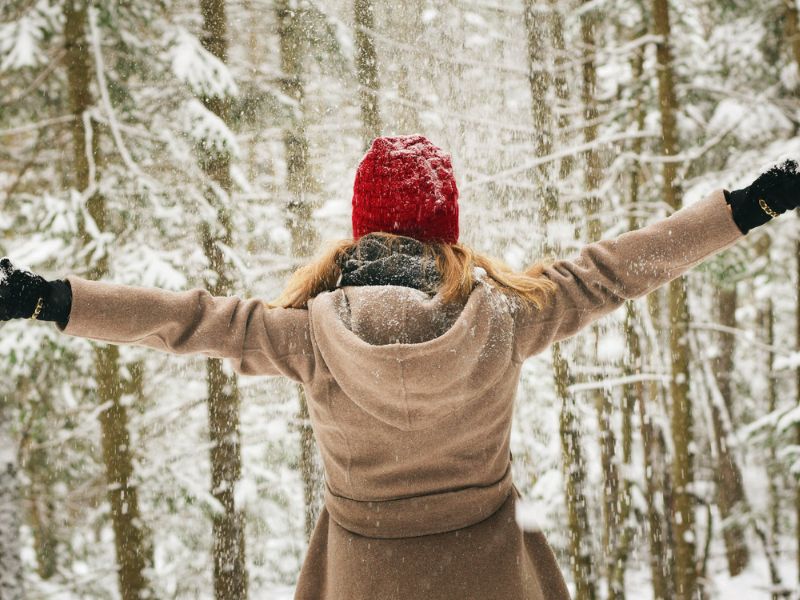 lady wearing pink winter coat and red beanie in a forest winter packing list
