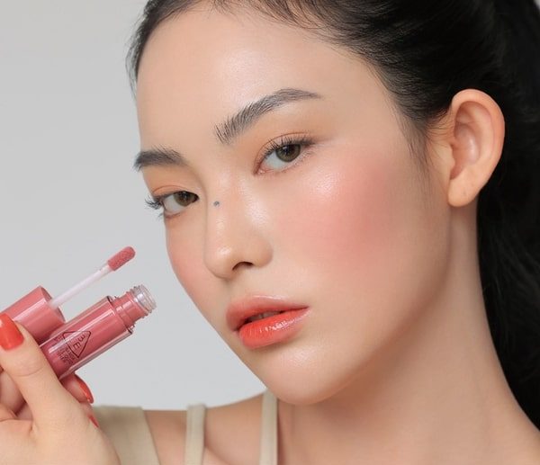 woman holding and wearing 3ce liquid blush