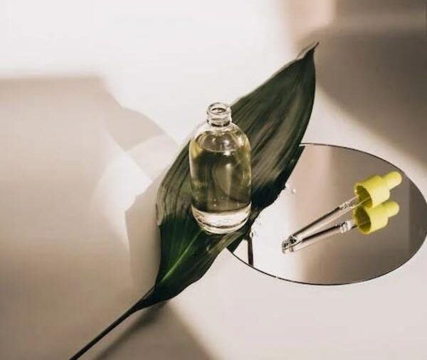 bottle of serum on a leaf with a mirror against white background
