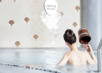 lady in bun dousing water with wooden pail at yunomori silk onsen in singapore