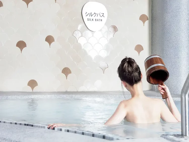 lady in bun dousing water with wooden pail at yunomori silk onsen in singapore