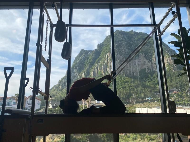 woman stretching on a reformer machine, with a beautiful scenary in the background - featuring one of the best pilates studio in singapore