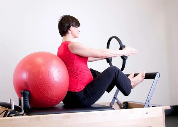 lady using the pilates wheel and ball on a reformer machine for her prenatal pilates class